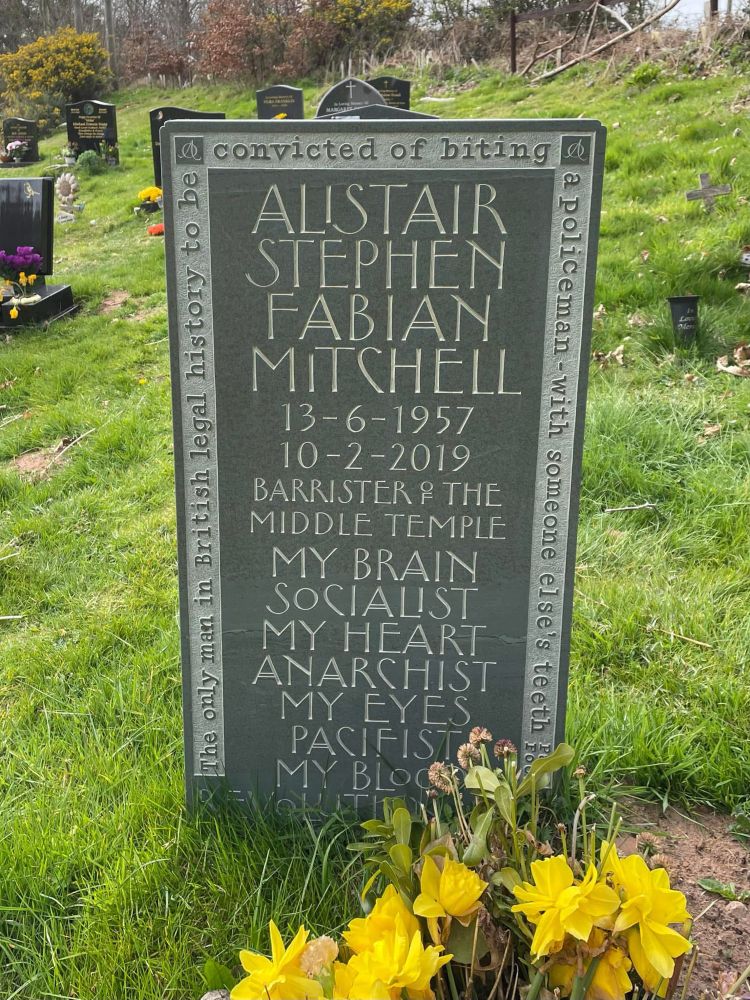 Gravestone inscribed: Alistair Stephen Fabian Mitchell. 13-6-1957, 10-2-2019. Barrister of the Middle Temple. My brain, socialist. My heart, anarchist. My eyes, pacifist. My blood, revolutionary.

Around the edge, the legend: The only man in British legal history to be convicted of biting a policeman with someone else’s teeth.